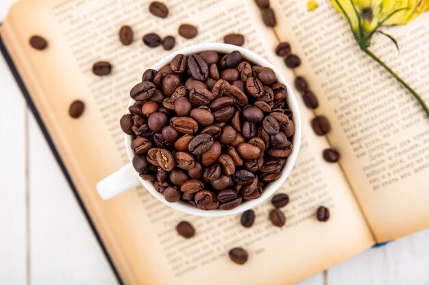 Top view of fresh coffee beans on a white cup on a white wooden background