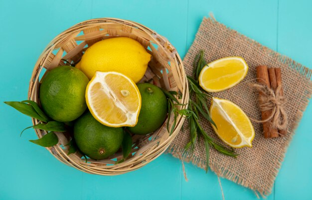 Top view of fresh and colorful lemons on bucket with slices of lemonnd green tarragon on sack cloth on blue