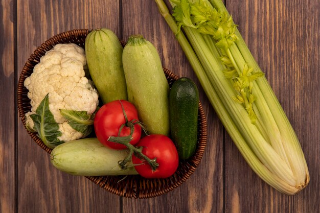 Top view of fresh colorful vegetables such as tomatoes zucchini cucumber and cauliflower on a bucket with celery isolated on a wooden wall