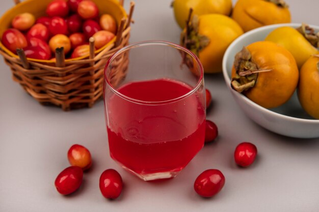 Top view of fresh cornelian fruit juice in a glass with cornelian fruits on a bucket on a grey wall