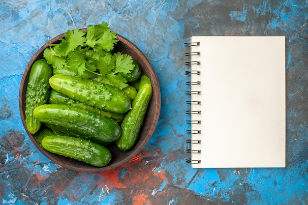 Top view fresh cucumbers inside plate with notepad on blue background photo color ripe salad food meal