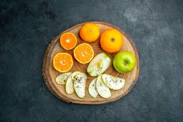 Вид сверху свежесрезанных яблок и апельсинов с порошком сушеной мяты на деревянной доске на черном столе