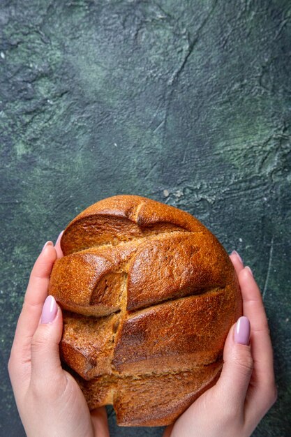 Вид сверху свежий темный хлеб с женскими руками на темном столе