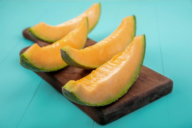 Top view of fresh and delicious cantaloupe melon slices on wooden kitchen board on blue
