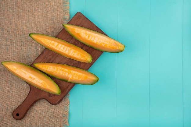 Foto gratuita vista dall'alto di fette di melone cantalupo fresche e deliziose sulla tavola di cucina in legno sul panno del sacco sul blu con lo spazio della copia