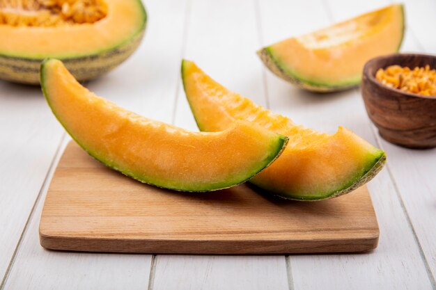 Top view of fresh and delicious cantaloupe melon slices on wooden kitchen board on white wood