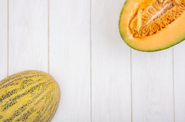 Top view of fresh and delicious halved and whole cantaloupe melon with seeds on white wood with copy space