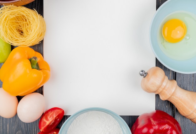 Top view of fresh egg yolk and white on a bowl with salt shaker with an orange bell pepper on a wooden background with copy space