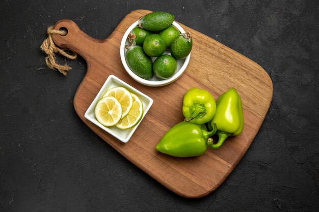 Вид сверху свежей фейхоа с зеленым болгарским перцем и лимоном на темной поверхности фруктовая мука из цитрусовых растений