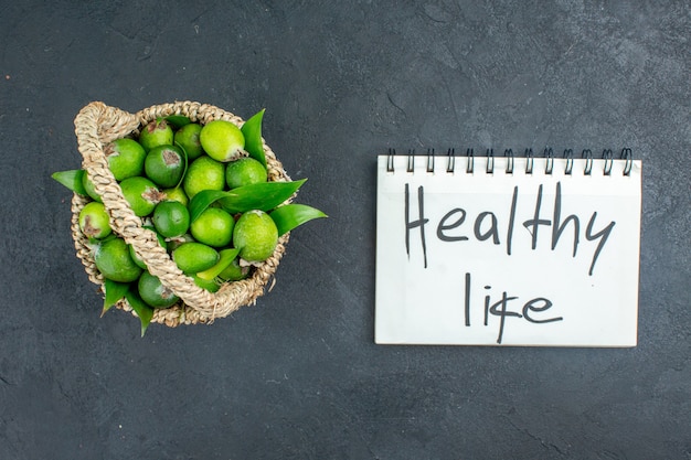 Free photo top view fresh feijoas in basket healthy life written on notebook on dark surface