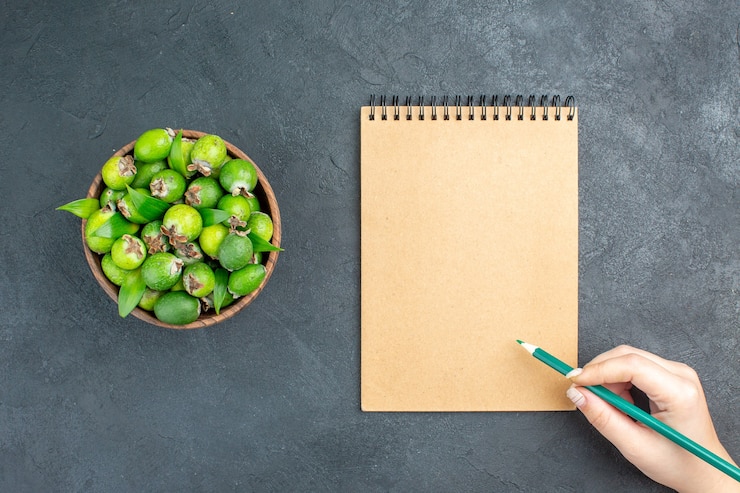 Free Photo top view fresh feijoas in bucket notepad green pencil in woman hand on dark surface