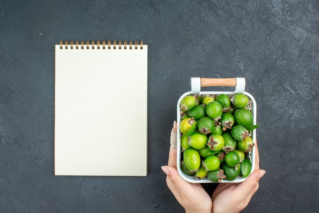 어두운 표면에 여성 손 메모장에 플라스틱 바구니에 상위 뷰 신선한 feijoas