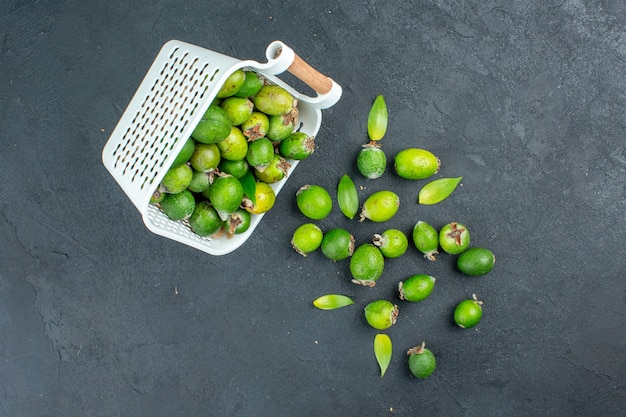 Top view fresh feijoas scattered from plastic basket on dark surface with copy place