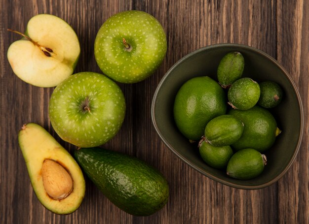 Top view of fresh feijoas with limes on a bowl with green apples and avocados isolated on a wooden surface