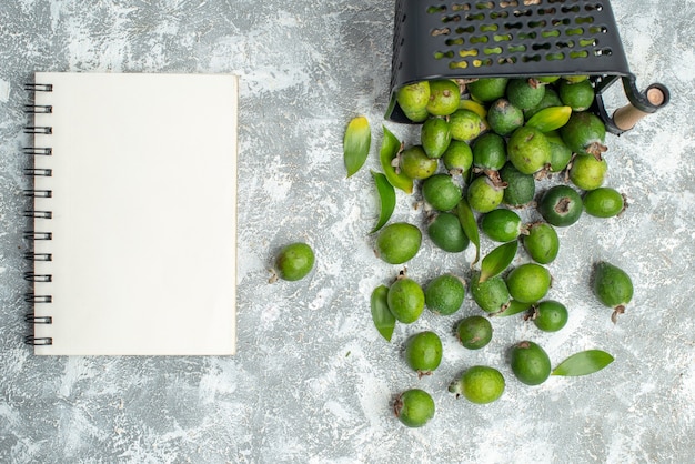 Top view fresh feykhoas scattered from basket notebook on grey surface