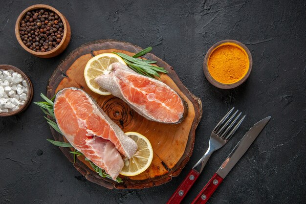 Top view fresh fish slices with lemon and seasonings on dark table