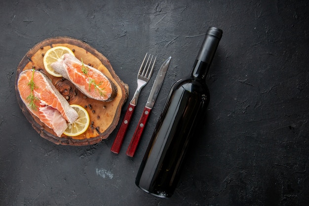 Top view fresh fish slices with lemon slices and cutlery on dark table