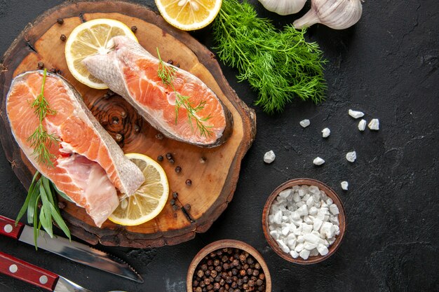 Top view fresh fish slices with lemon slices and garlic on the dark table