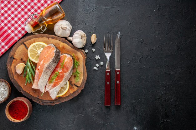 Top view fresh fish slices with lemon slices garlic and seasonings on a dark table