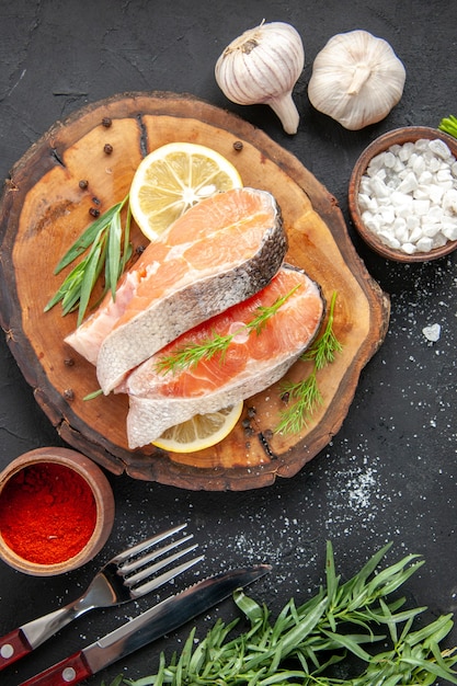 Top view fresh fish slices with lemon slices and seasonings on a dark table