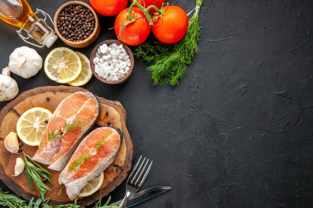 Top view fresh fish slices with seasonings and lemon slices on dark table