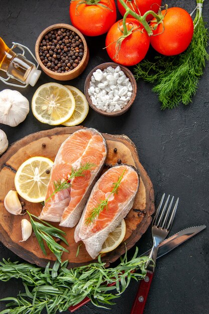 暗いテーブルに調味料とレモンスライスを添えた新鮮な魚のスライスの上面図
