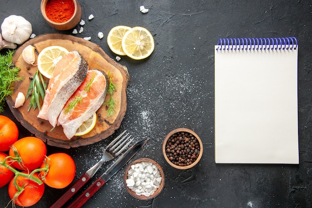 暗いテーブルの上のトマト調味料とレモンスライスと新鮮な魚のスライスの上面図