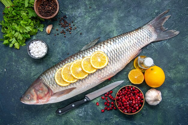 Top view fresh fish with lemon slices knife pomegranate seeds bowl lemon on kitchen table