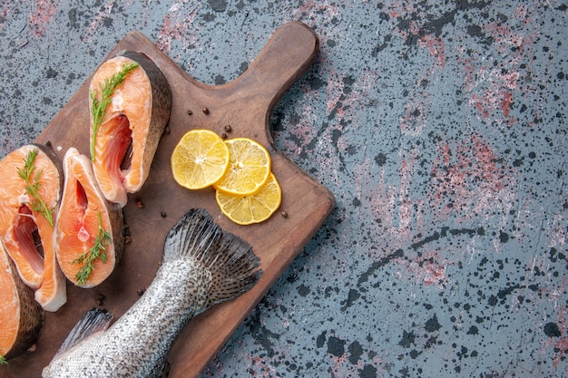 Top view of fresh fishes lemon slices greens pepper on wooden cutting board on blue black mix colors table