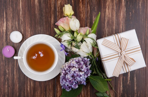 Top view of fresh flowers like gardenzia tulip roses with a cup of tea with gift box isolated on a wooden background