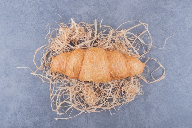 Top view of fresh French croissant on decorative straw over grey background.