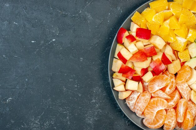 Top view fresh fruit salad sliced bananas apples and oranges on dark background