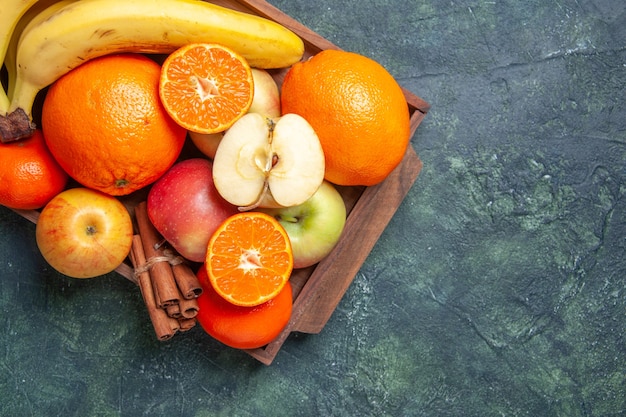 Top view fresh fruits bananas apples oranges cinnamon sticks on wooden tray on dark background