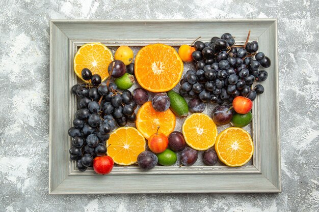 Top view fresh fruits composition grapes oranges plums and feijoa on white table