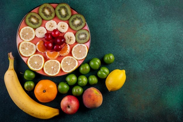신선한 과일 레몬 귤 바나나 복숭아 사과 녹색 신 체리 자 두와 어둠에 접시에 빨간 체리와 얇게 썬 과일의 상위 뷰