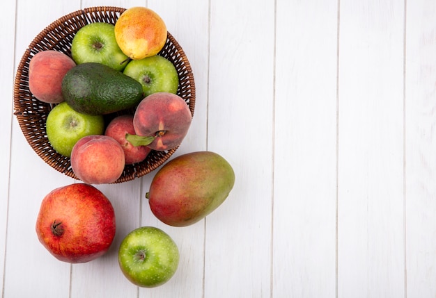 Top view of fresh fruits like apples peaches pear on bucket with pomegranate mango isolated on white