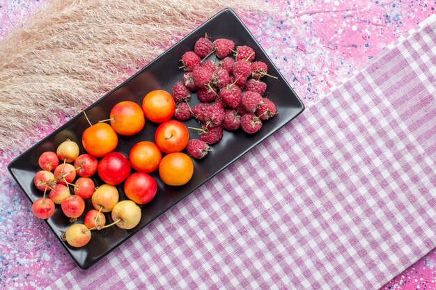 Top view of fresh fruits raspberries and plums inside black form on pink surface