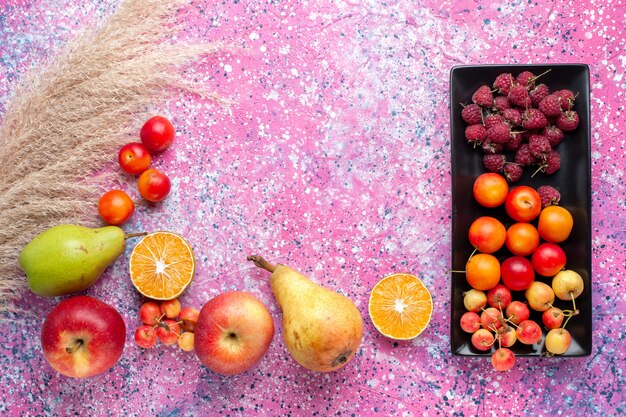 Top view of fresh fruits raspberries and plums inside black form on the pink surface