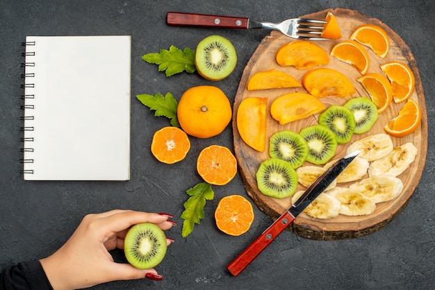 黒いテーブルにオレンジを持って木製トレイの手にセットされた新鮮な果物の上面図