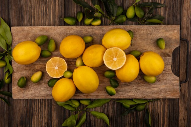 Вид сверху свежих фруктов, таких как кинканы и лимоны, на деревянной кухонной доске на деревянной стене