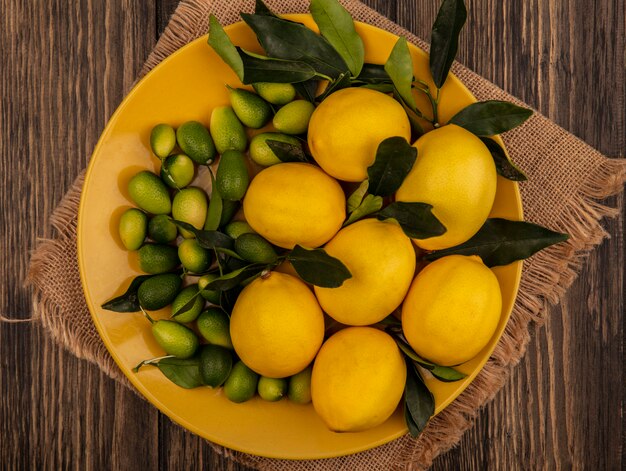 나무 표면에 자루 천에 노란색 접시에 레몬과 킨칸과 같은 신선한 과일의 상위 뷰