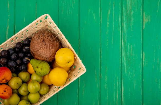 Vista dall'alto di frutta fresca come peachescoconutgreen ciliegia prugne su un secchio su uno sfondo verde con copia spazio