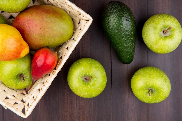 Top view of fresh fruits such as pear apple mango on bucket with green apples on wood