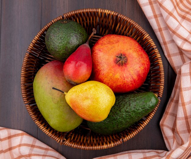 Top view of fresh fruits such as pear lemon mango pomegranate on bucket with checked tablecloth on wood