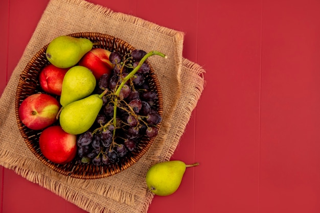 복사 공간이 빨간색 배경에 자루 천에 나무 그릇에 배 복숭아 포도와 같은 신선한 과일의 상위 뷰