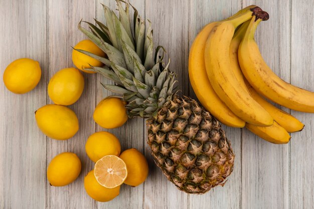 Top view of fresh fruits such as pineapple bananas and lemons isolated on a grey wooden surface