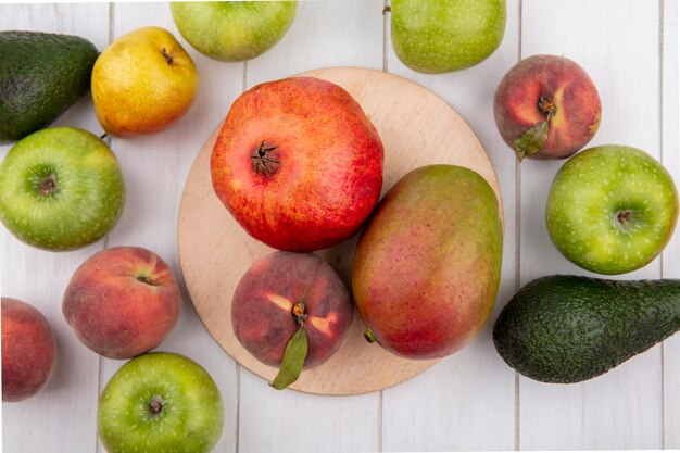 Top view of fresh fruits such as pomegranate peach mango on kitchen board with green apples avocados peach pears isolated on white