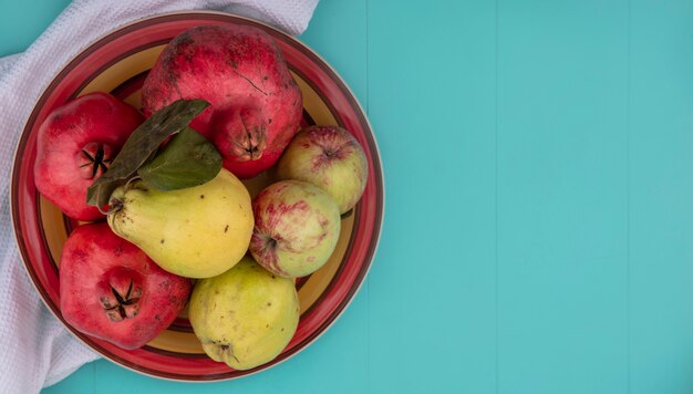 Top view of fresh fruits such as pomegranate quince and apples on a bowl on a white cloth on a blue background with copy space