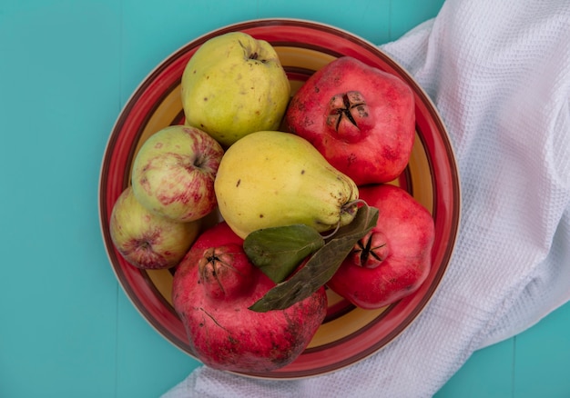 Top view of fresh fruits such as pomegranate quince and apples on a bowl on a white cloth on a blue background