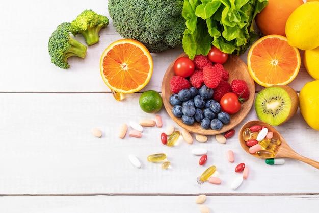 Top view of fresh fruits and vegetables with different medicine on a wooden spoon